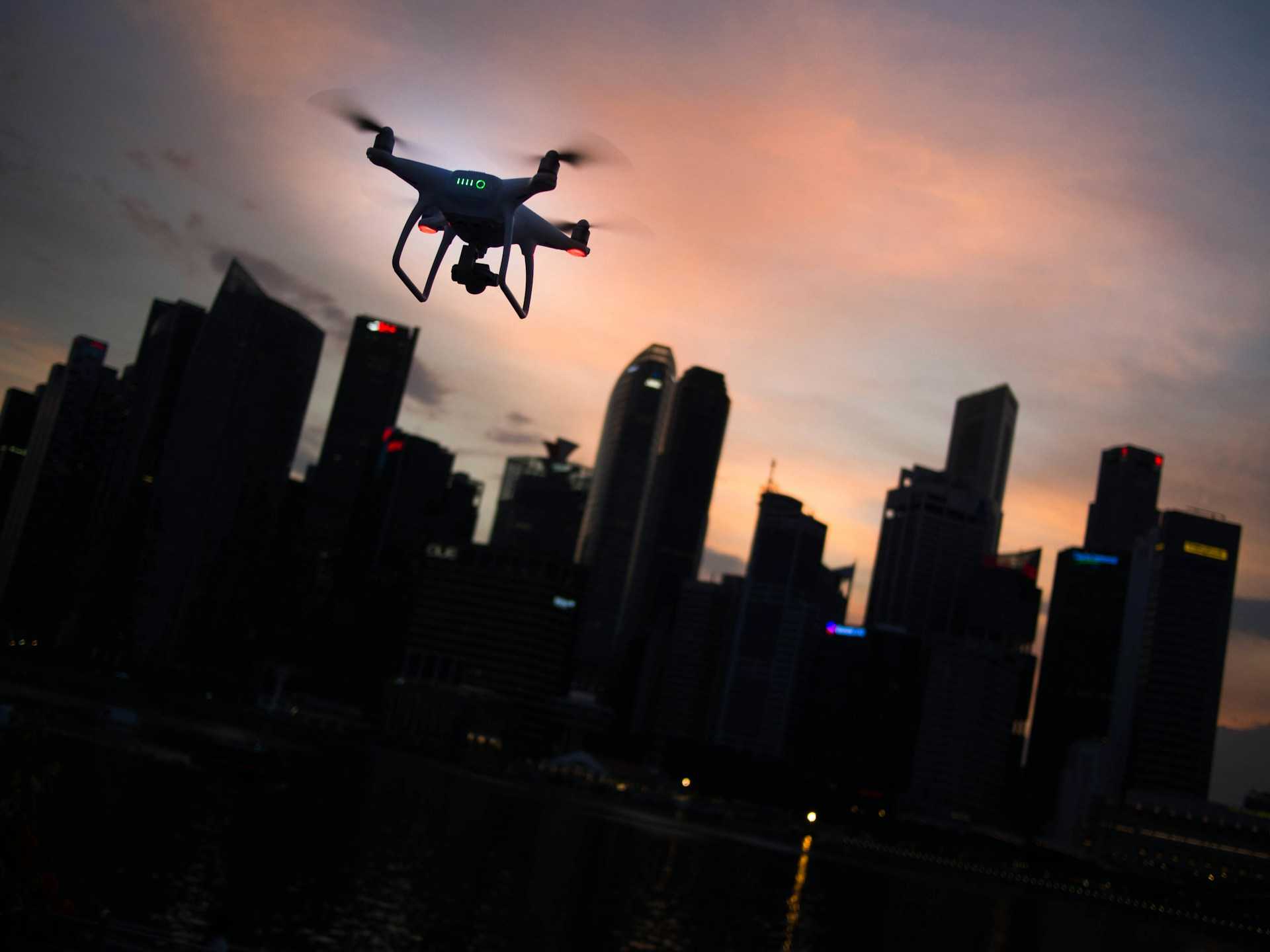 A quadcopter drone flying over a city at dusk.