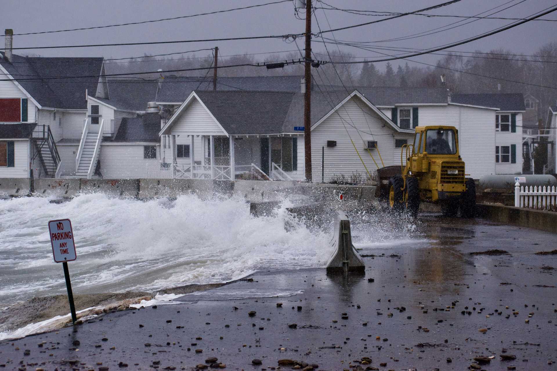 Coastal flooding during a storm, with waves crashing over a seawall near homes, highlighting the impacts of climate change on coastal communities.